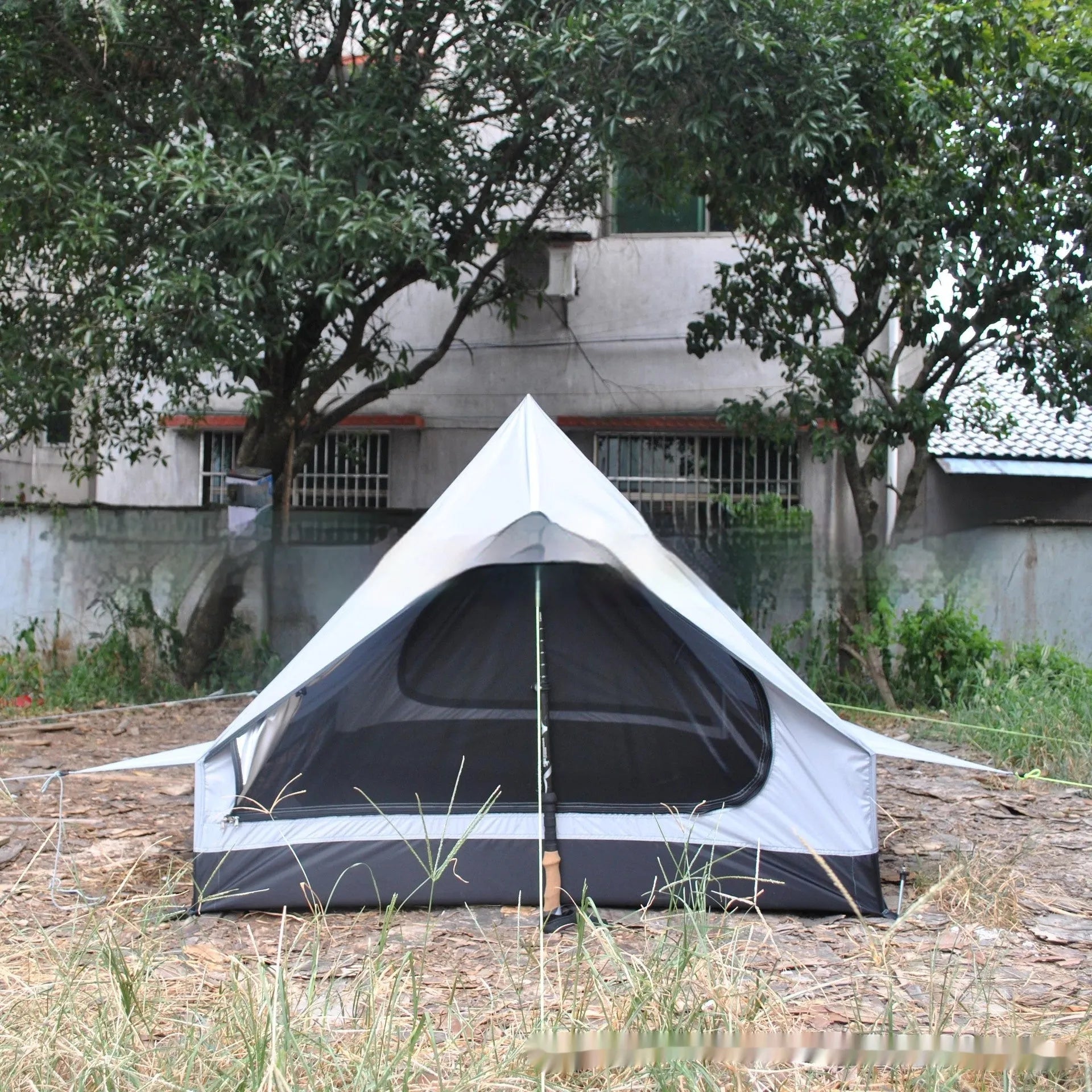 Brown A-line hiking tent set up with trekking poles in a forest clearing.