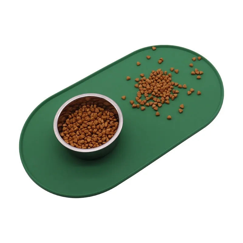 Green silicone cat feeding placemat with food and water bowls on it, on a wooden floor.