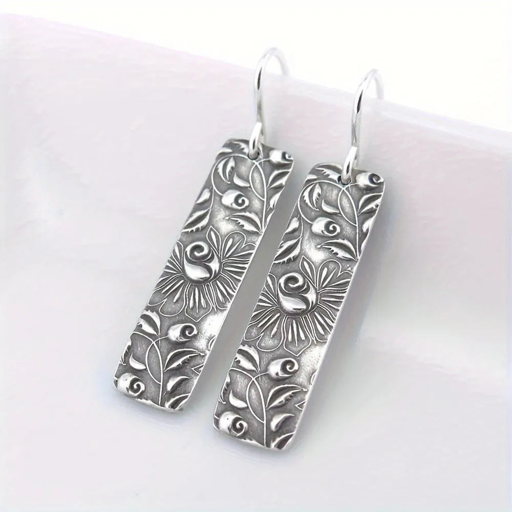 Silver retro geometric long strip carved vine earrings made from zinc alloy on a plain background