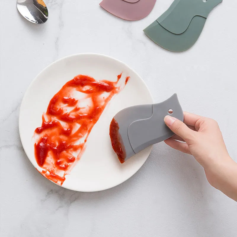 Penguin shape soft blade scraper 11x7cm in green cleaning a plate with sauce residue
