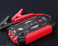 Compact red car battery jump starter unit with cables and clips on a dark background.