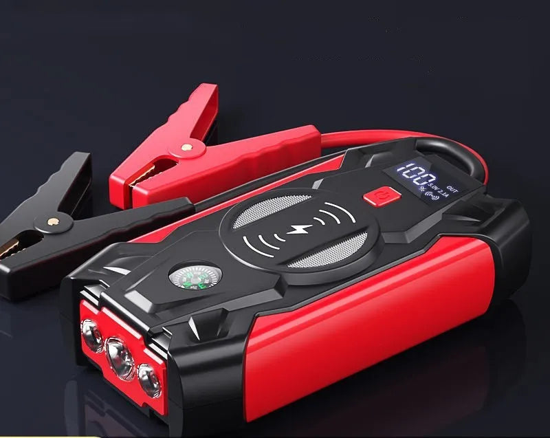 Compact red car battery jump starter unit with cables and clips on a dark background.
