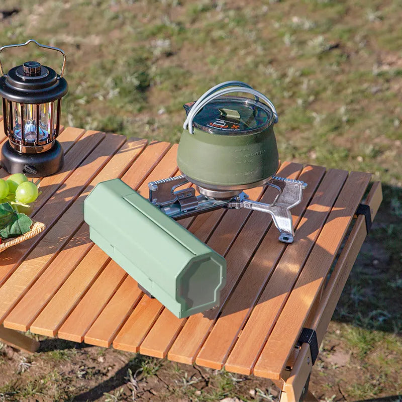 Green folding camping gas stove with burner, serrated bracket, and anti-slip feet on a tabletop