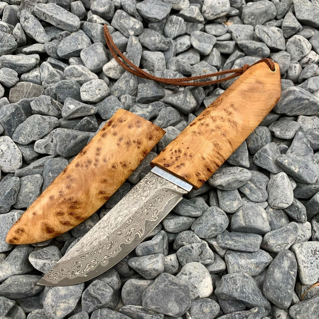 Damascus pattern steel short knife with VG10 steel blade and Thuja wood handle on wooden surface