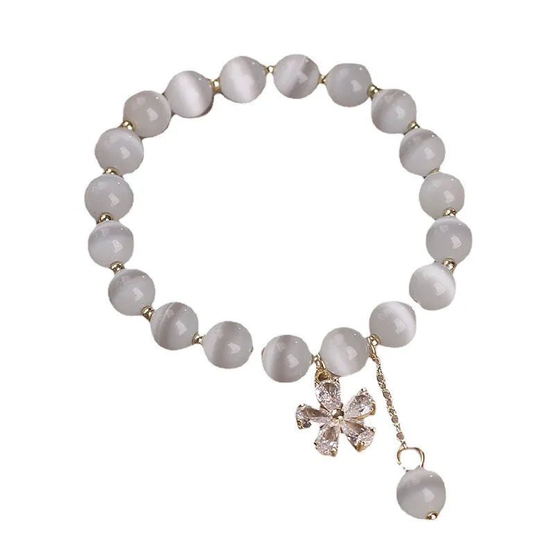 Close-up of a white cat's eye crystal bracelet with a flower tassel pendant and a morganite safety buckle.