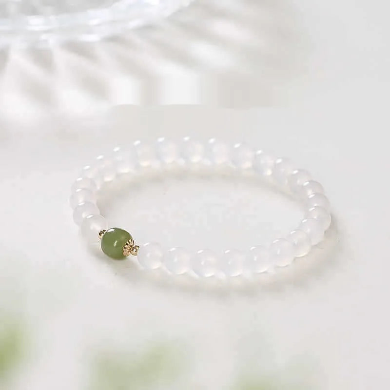 Handmade white agate and cinnabar bracelet with letter charms on a wrist.