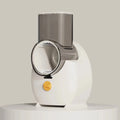 Electric vegetable slicer in white with feeding port, pressing rod, and blade barrel on a kitchen counter