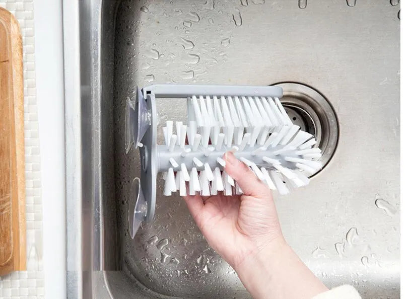 Grey suction cup brush with double-head design and two suction cups on a kitchen wall