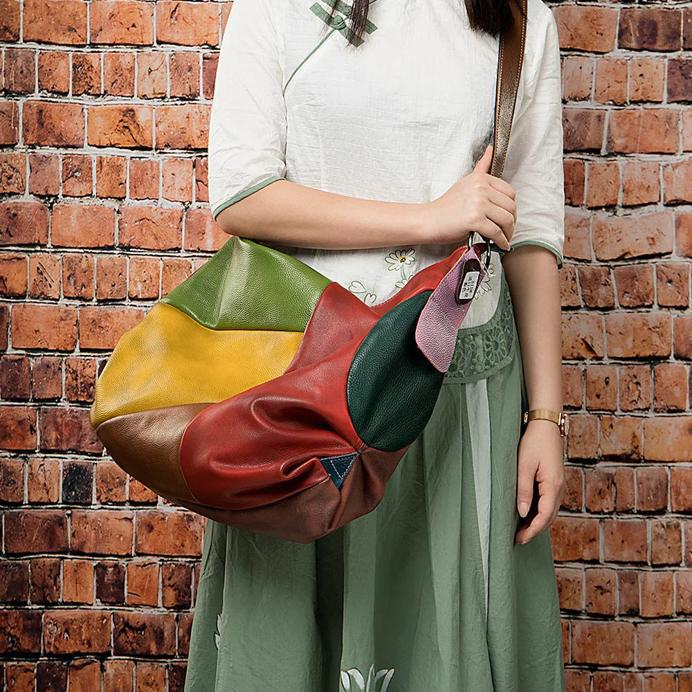 Brown cowhide leather crossbody travel bag with visible stitching, shown next to a laptop and iPad for scale.
