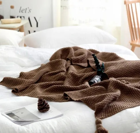 Nordic style acrylic knit blanket with fringed ball trim in a choice of four colours on a sofa.
