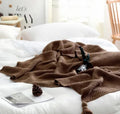Nordic style acrylic knit blanket with fringed ball trim in a choice of four colours on a sofa.