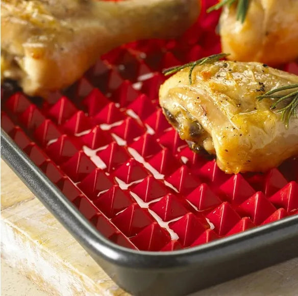 Red non-stick silicone pyramid cooking mat with grid on a baking tray for oven or BBQ use