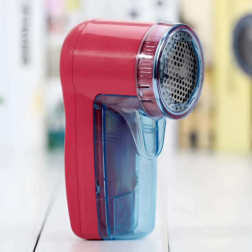 Compact white electric lint remover for clothing on a table next to a grey sweater.