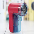 Compact white electric lint remover for clothing on a table next to a grey sweater.
