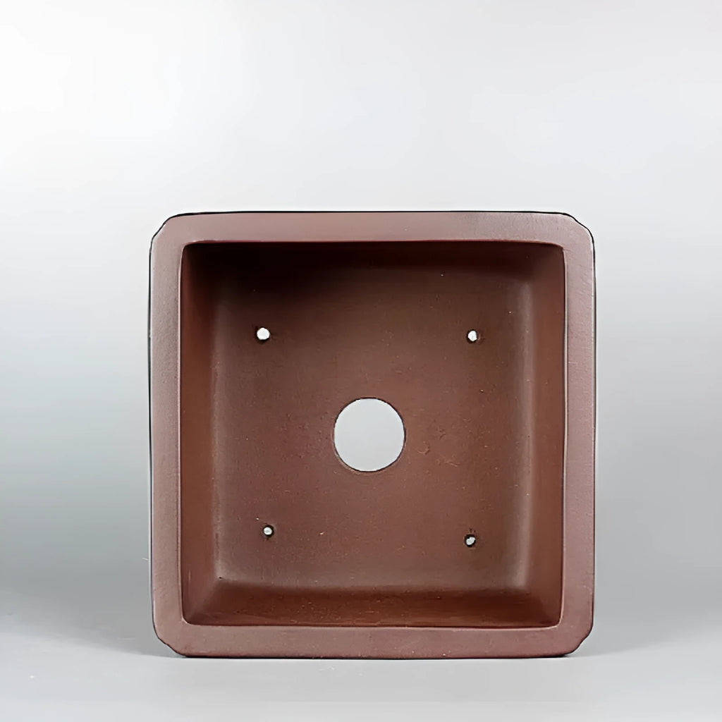 Brown handmade purple clay square flower pot with classical design on a wooden surface.