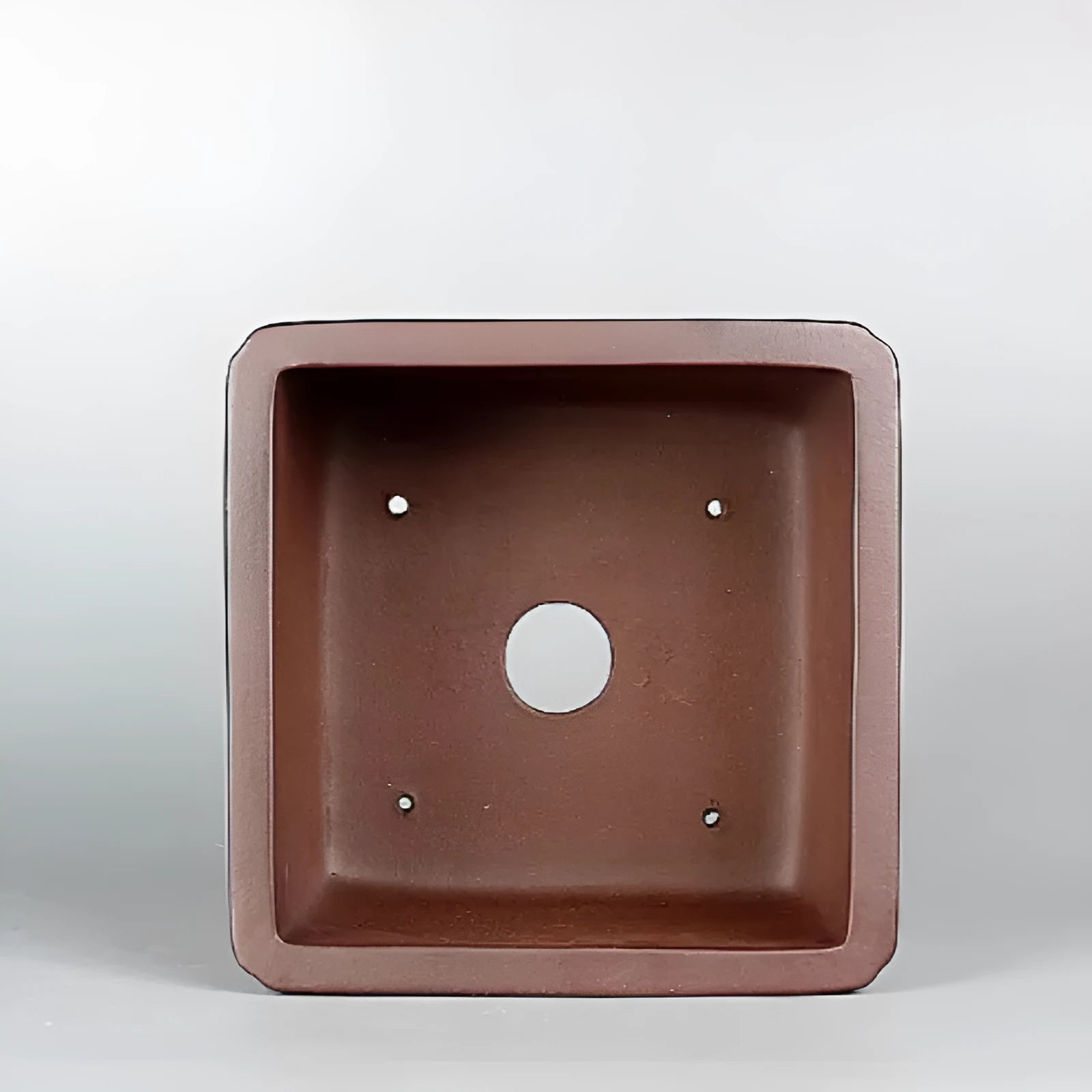 Brown handmade purple clay square flower pot with classical design on a wooden surface.