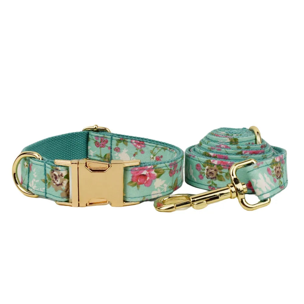 Cloth dog collar with green background and detachable cute bow next to matching leash and vest on a white surface