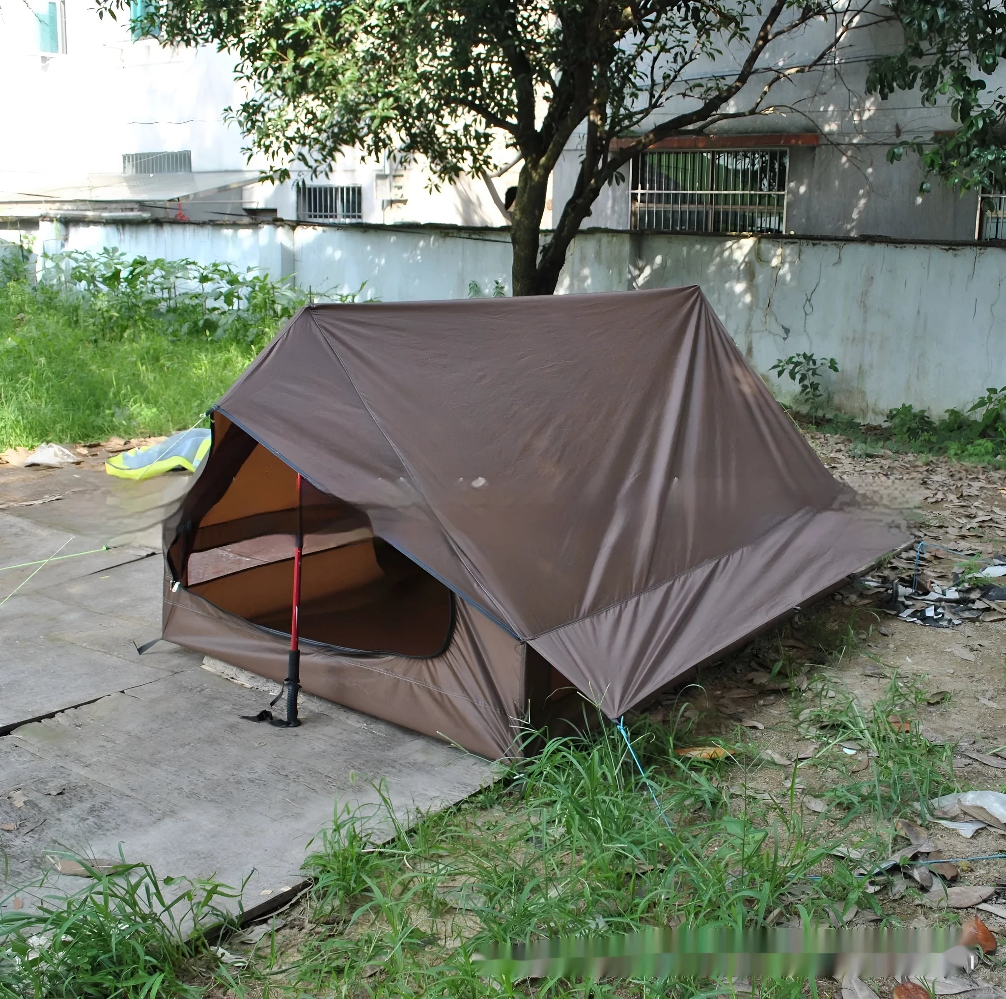 Brown A-line hiking tent set up with trekking poles in a forest clearing.