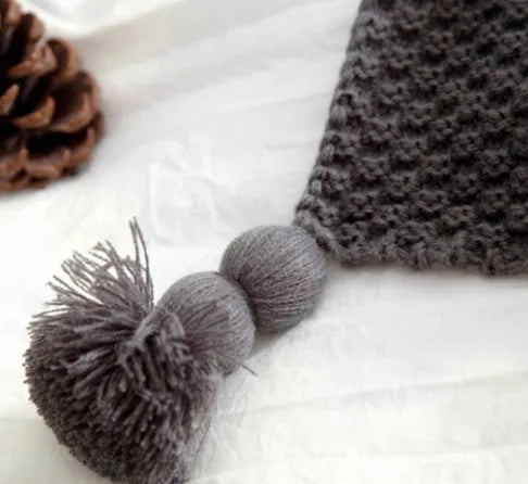 Nordic style acrylic knit blanket with fringed ball trim in a choice of four colours on a sofa.