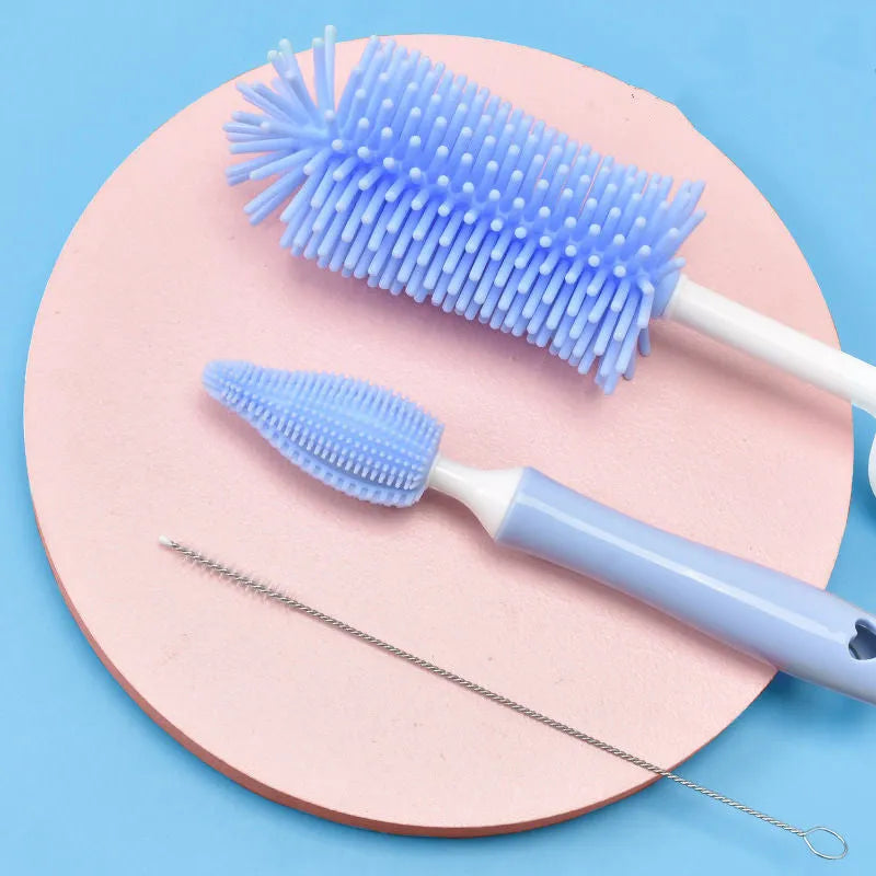 Three-piece silicone baby bottle brush set in pink, blue, and yellow with straw cleaning tool
