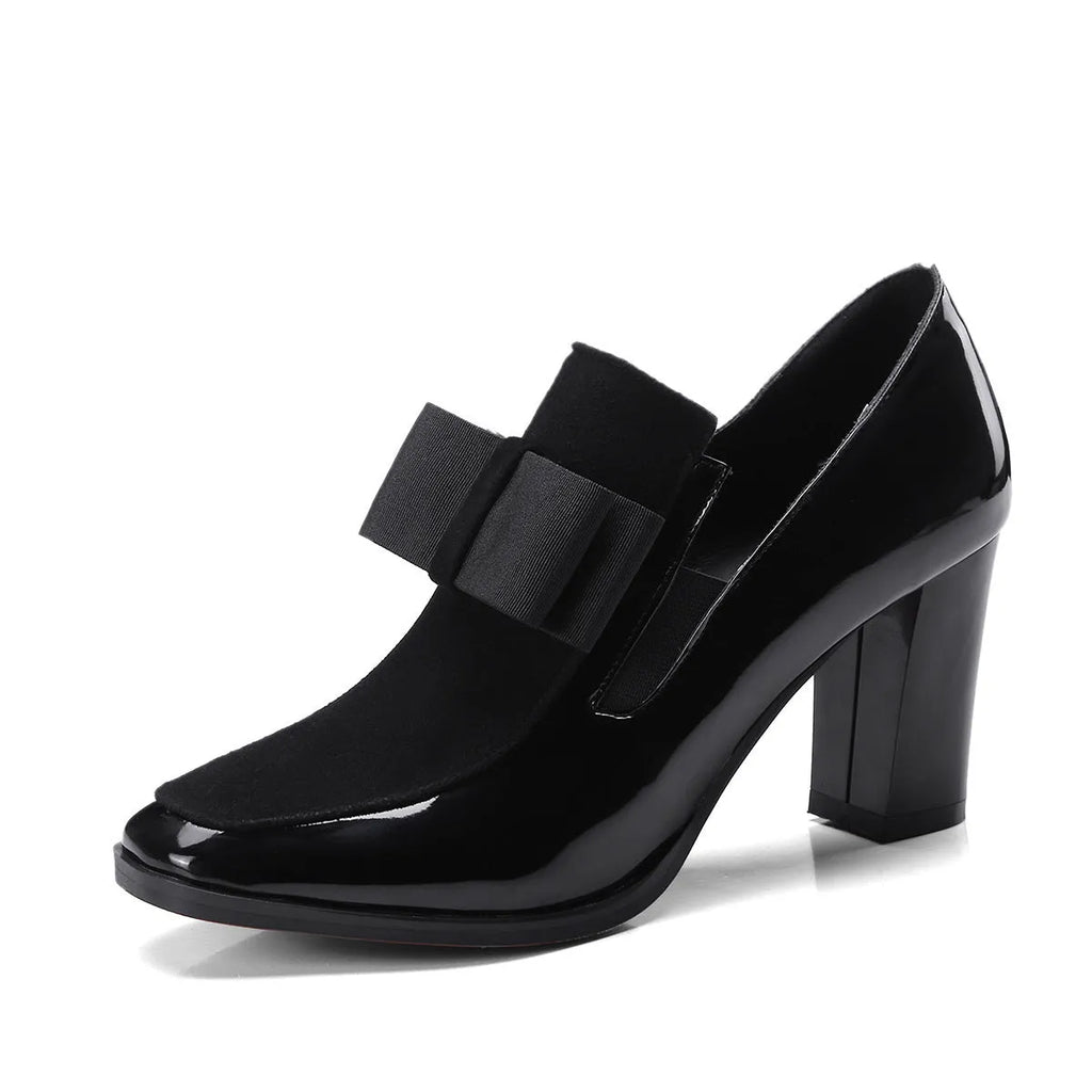 Black patent leather women's high heels with a thick super high heel and square toe on a plain background.