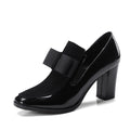 Black patent leather women's high heels with a thick super high heel and square toe on a plain background.