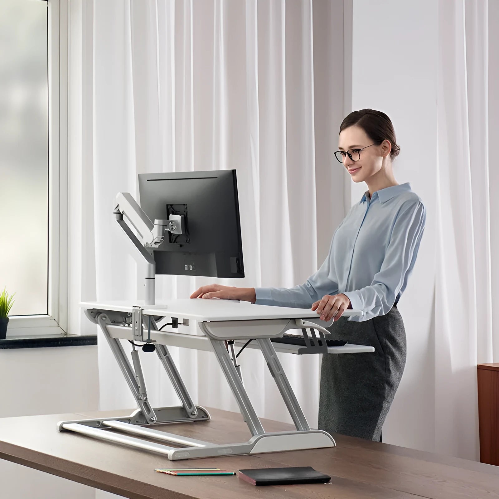 Adjustable lifting computer monitor stand in silver on a desk with a screen placed on top