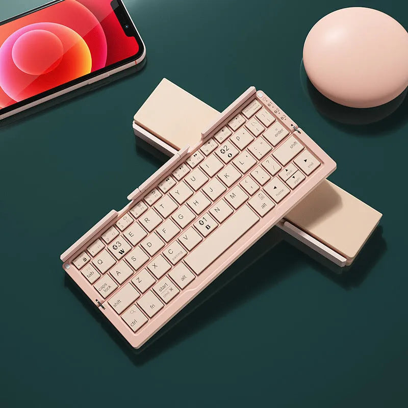 Silver white mini folding Bluetooth keyboard open next to a smartphone on its integrated stand.