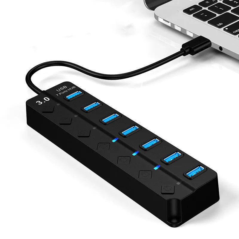 Black 7-port USB 3.0 hub with external power supply on a desktop.