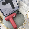 Black handheld electric fascia gun muscle massager with metal head on a grey background.