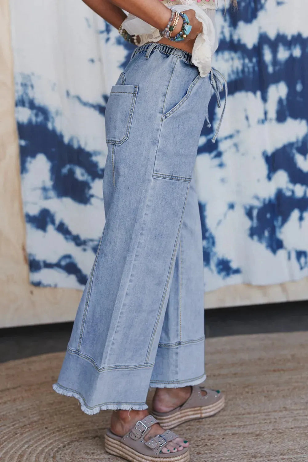 Beau Blue wide leg denim trousers on a hanger, showing drawstring waist, seam detailing, and raw hem.