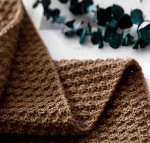 Nordic style acrylic knit blanket with fringed ball trim in a choice of four colours on a sofa.