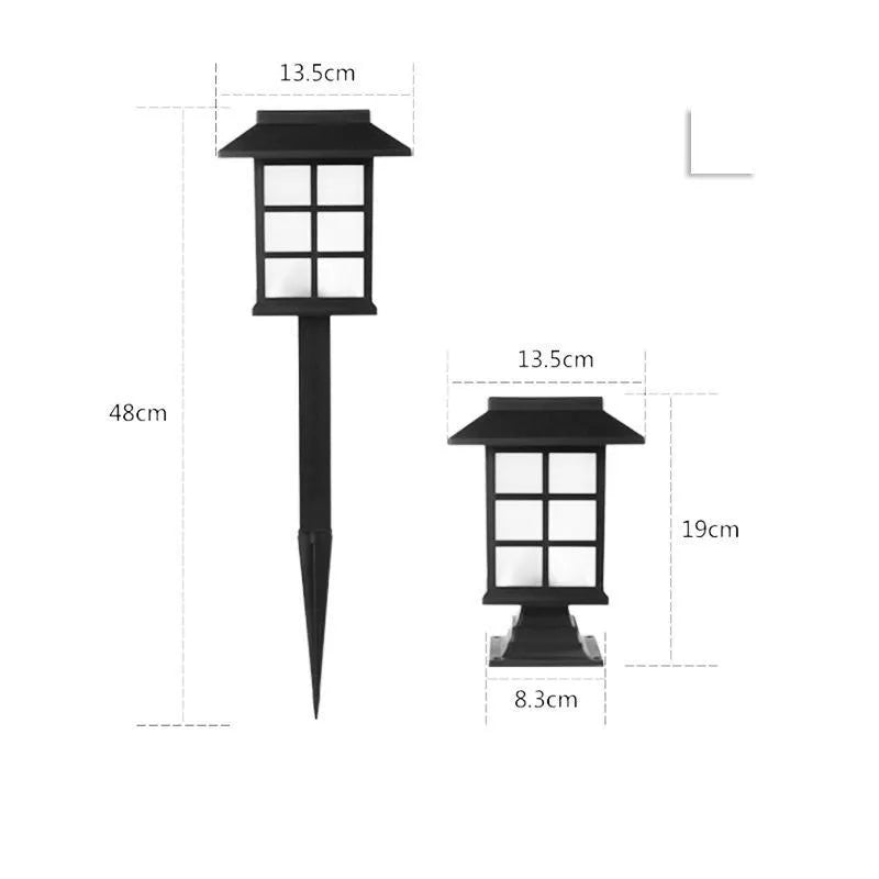 Solar outdoor LED lawn light with black body and white light through windows, set in a garden flower bed