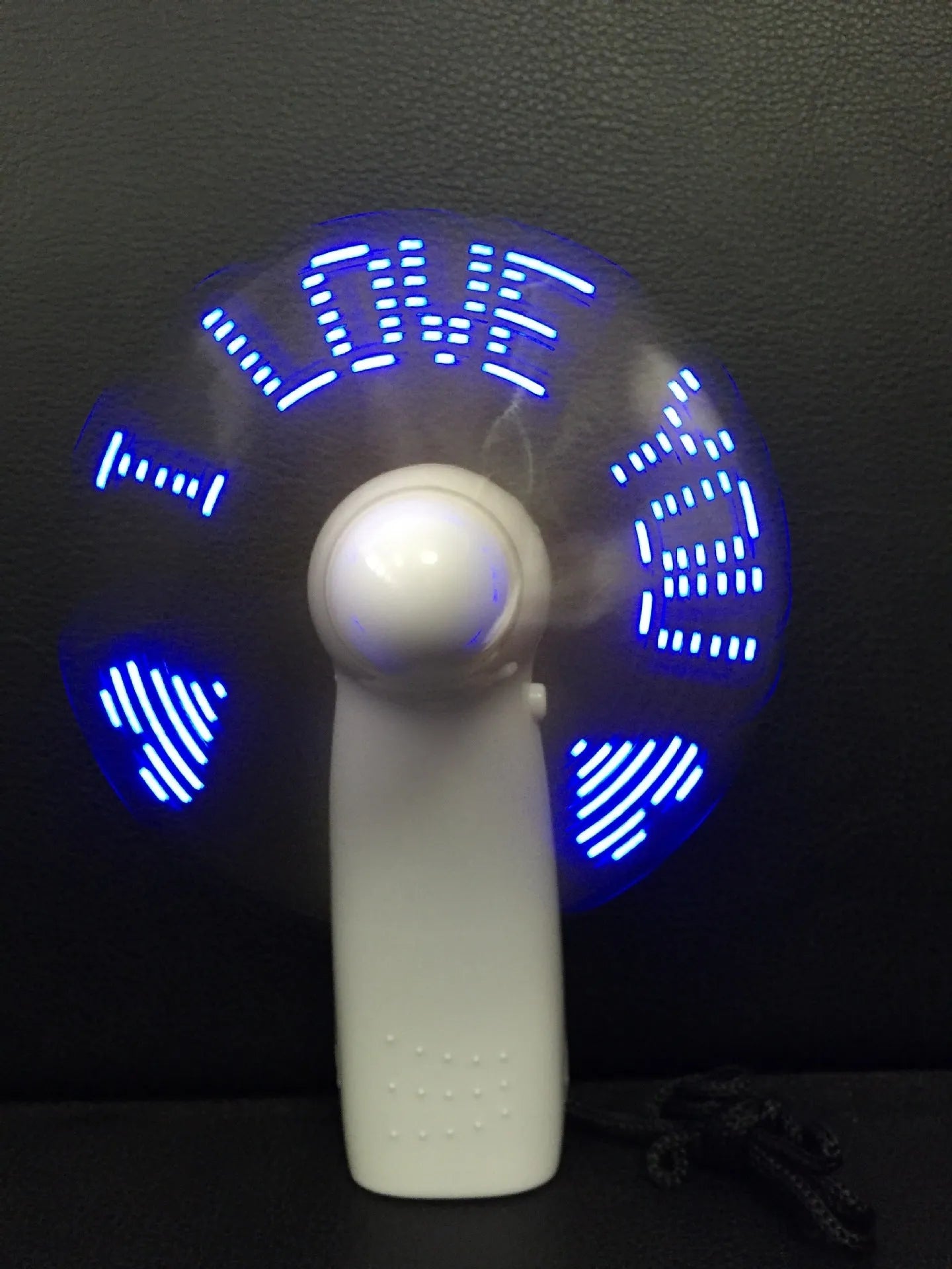 White handheld mini fan displaying blue and red LED 'I love you' pattern, shown next to a ruler for scale.
