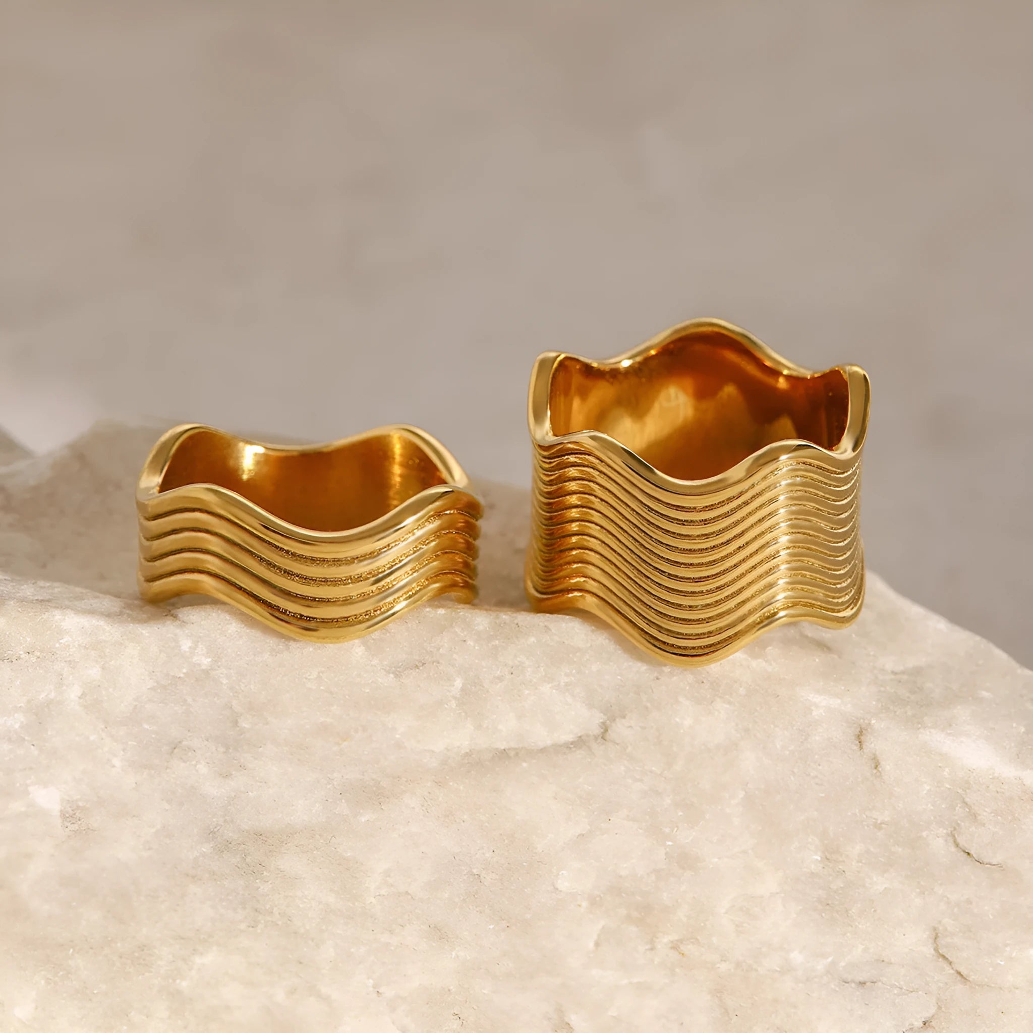 Stainless steel ring with a wide geometric wave design in a gold or silver finish.