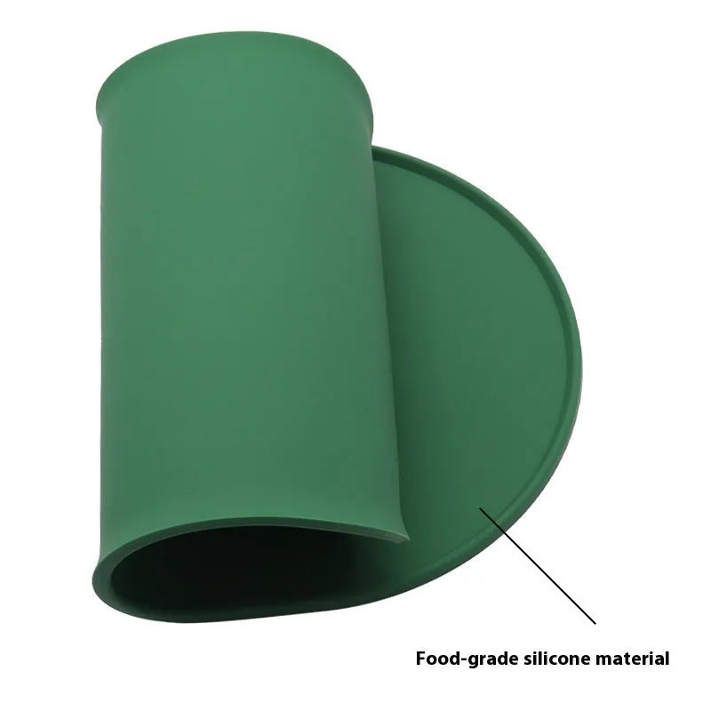 Green silicone cat feeding placemat with food and water bowls on it, on a wooden floor.