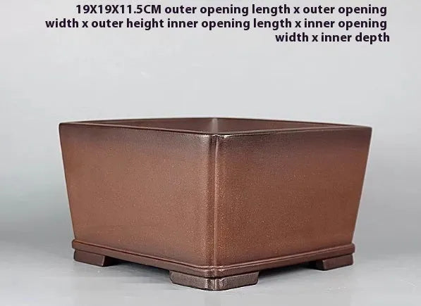 Brown handmade purple clay square flower pot with classical design on a wooden surface.