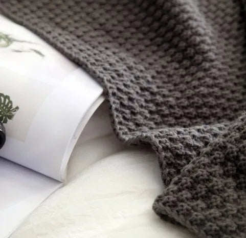 Nordic style acrylic knit blanket with fringed ball trim in a choice of four colours on a sofa.