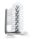 Grey suction cup brush with double-head design and two suction cups on a kitchen wall