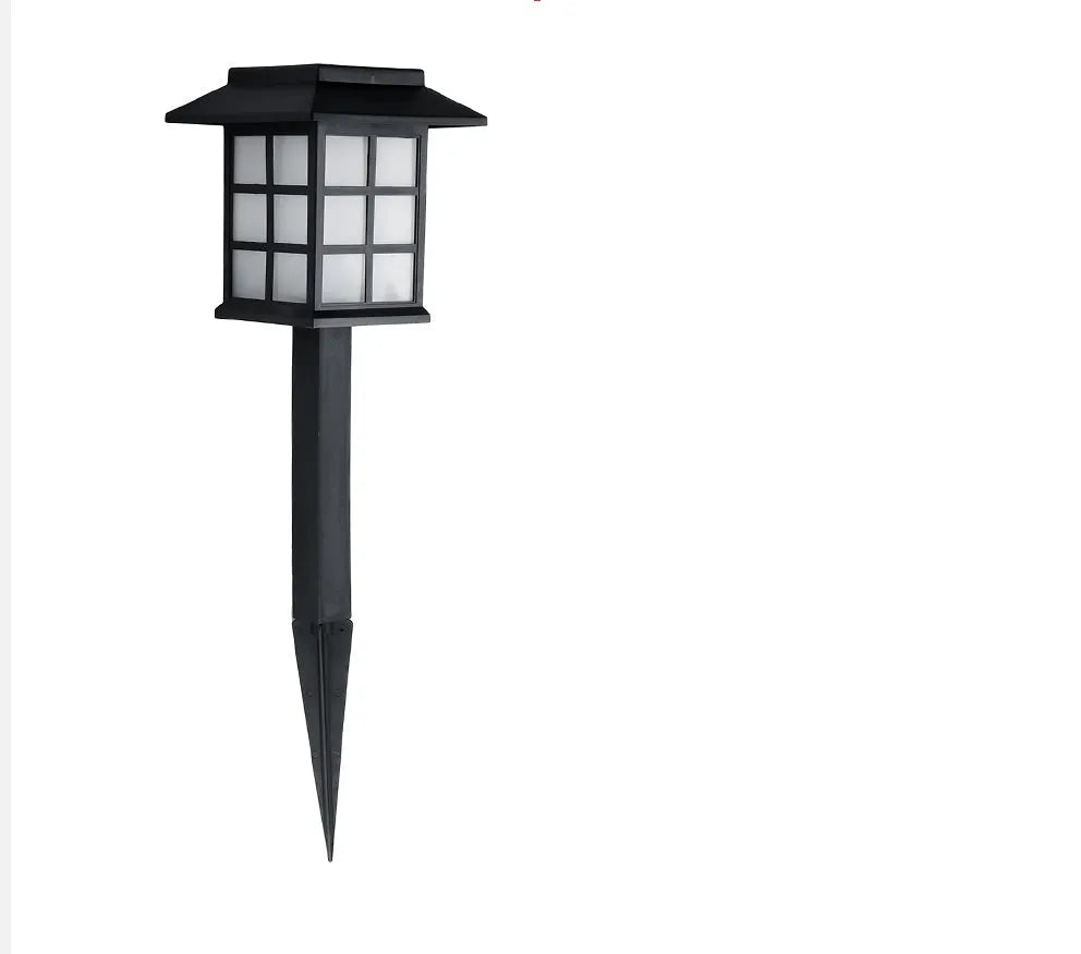 Solar outdoor LED lawn light with black body and white light through windows, set in a garden flower bed