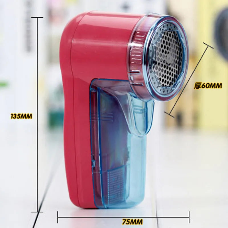 Compact white electric lint remover for clothing on a table next to a grey sweater.