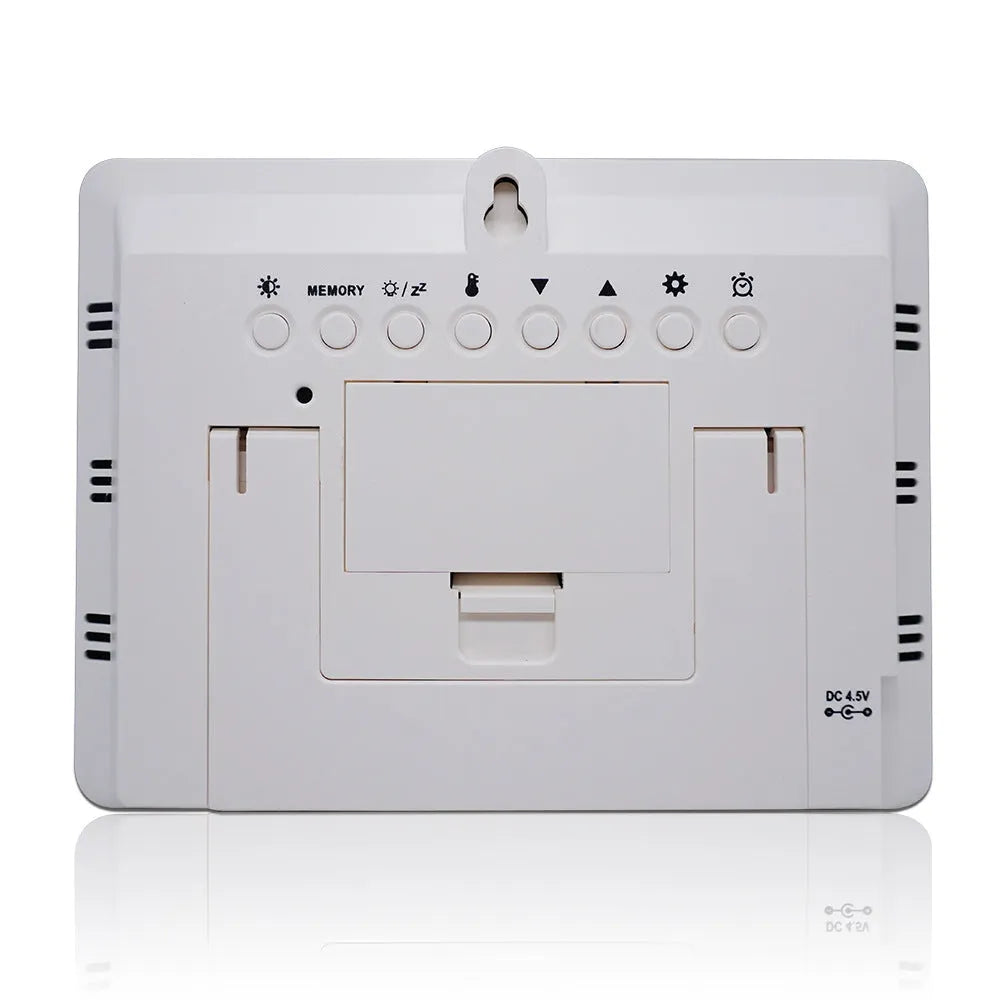 Rectangular black digital weather station with LCD display showing time, temperature, and weather icons on a desk.