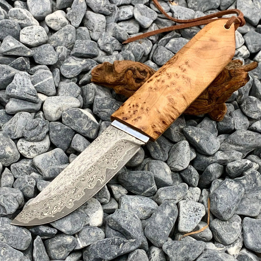 Damascus pattern steel short knife with VG10 steel blade and Thuja wood handle on wooden surface