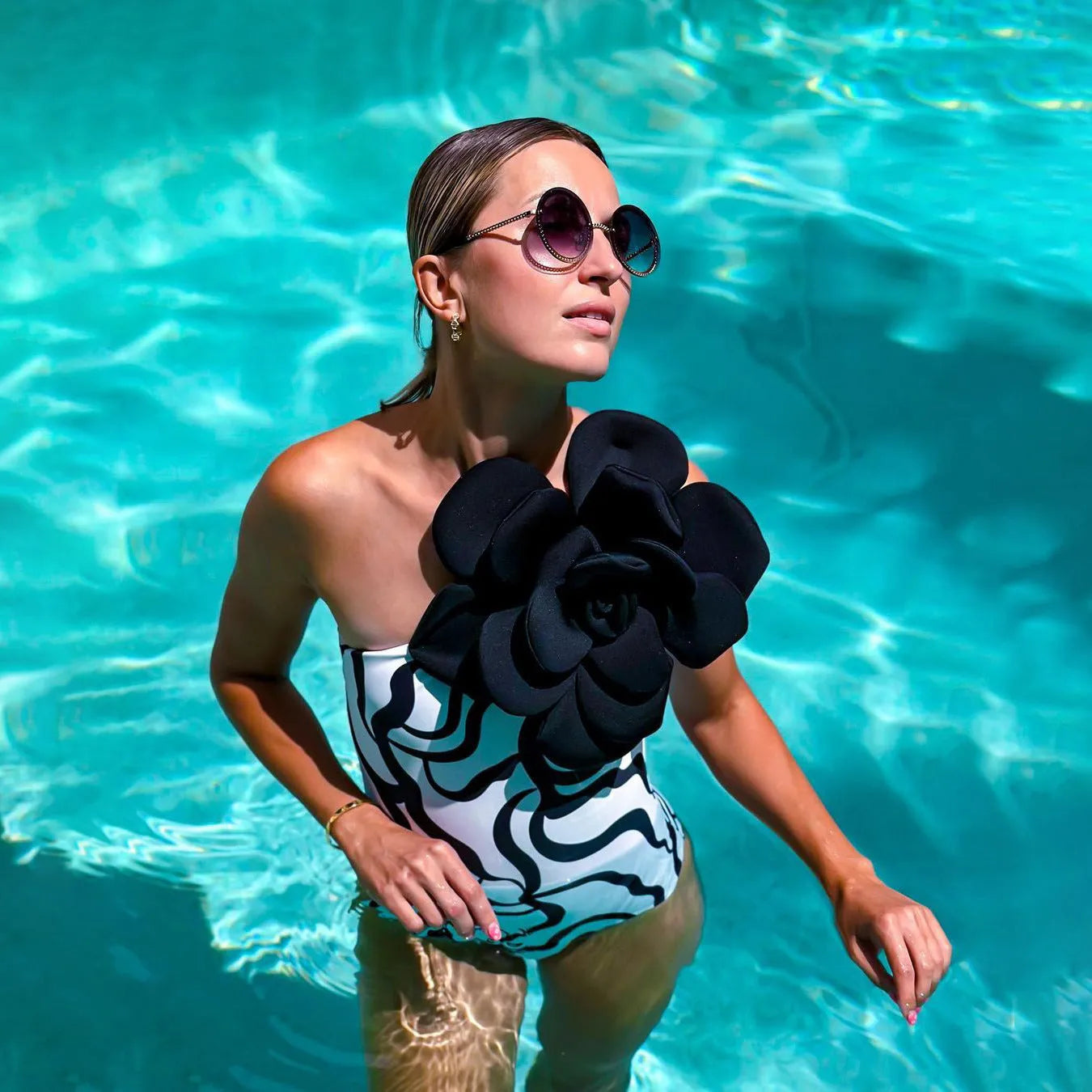 Form-fitting one-piece swimsuit with three-dimensional floral decoration on solid colour fabric.