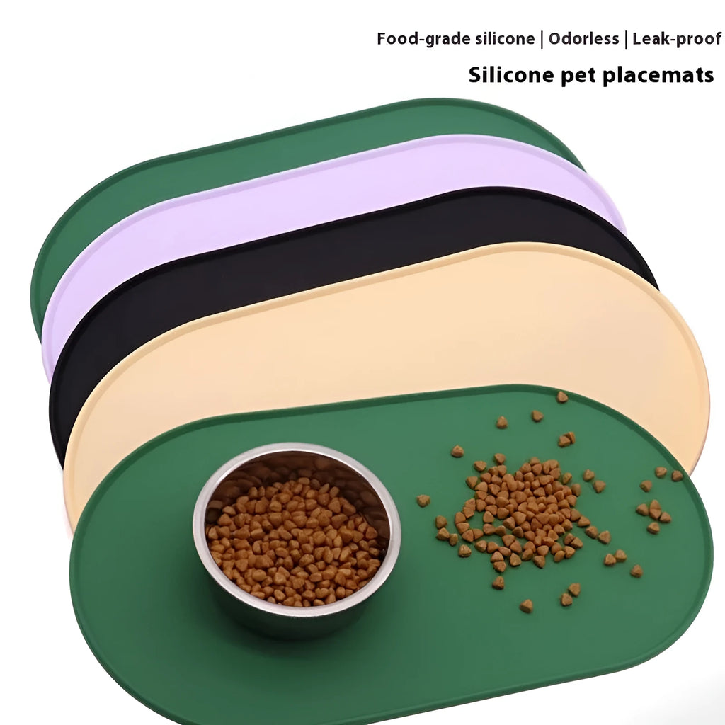 Green silicone cat feeding placemat with food and water bowls on it, on a wooden floor.