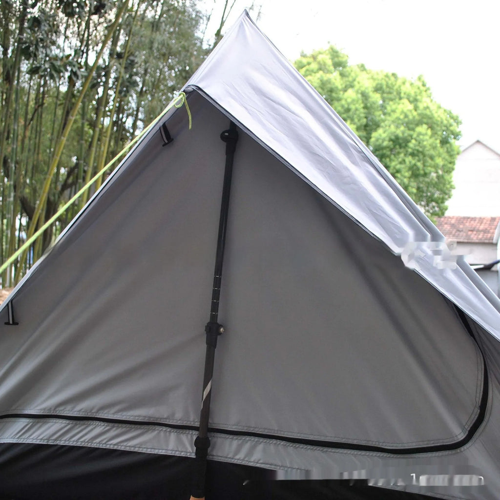 Brown A-line hiking tent set up with trekking poles in a forest clearing.