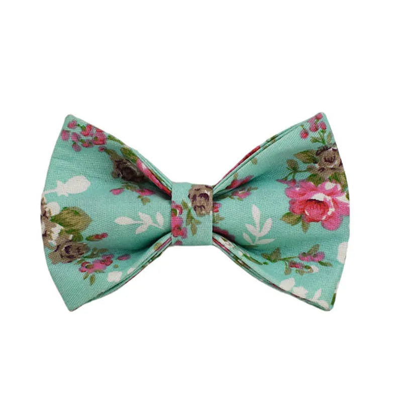 Cloth dog collar with green background and detachable cute bow next to matching leash and vest on a white surface