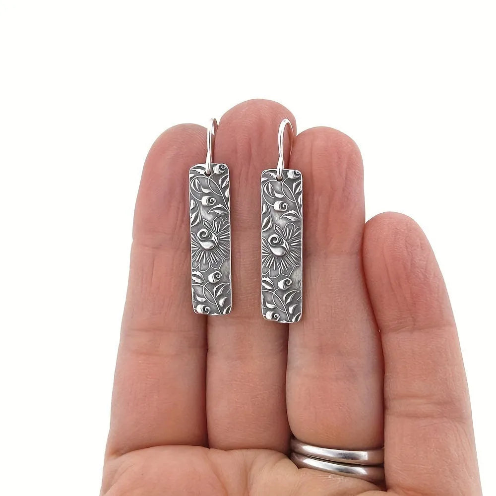 Silver retro geometric long strip carved vine earrings made from zinc alloy on a plain background