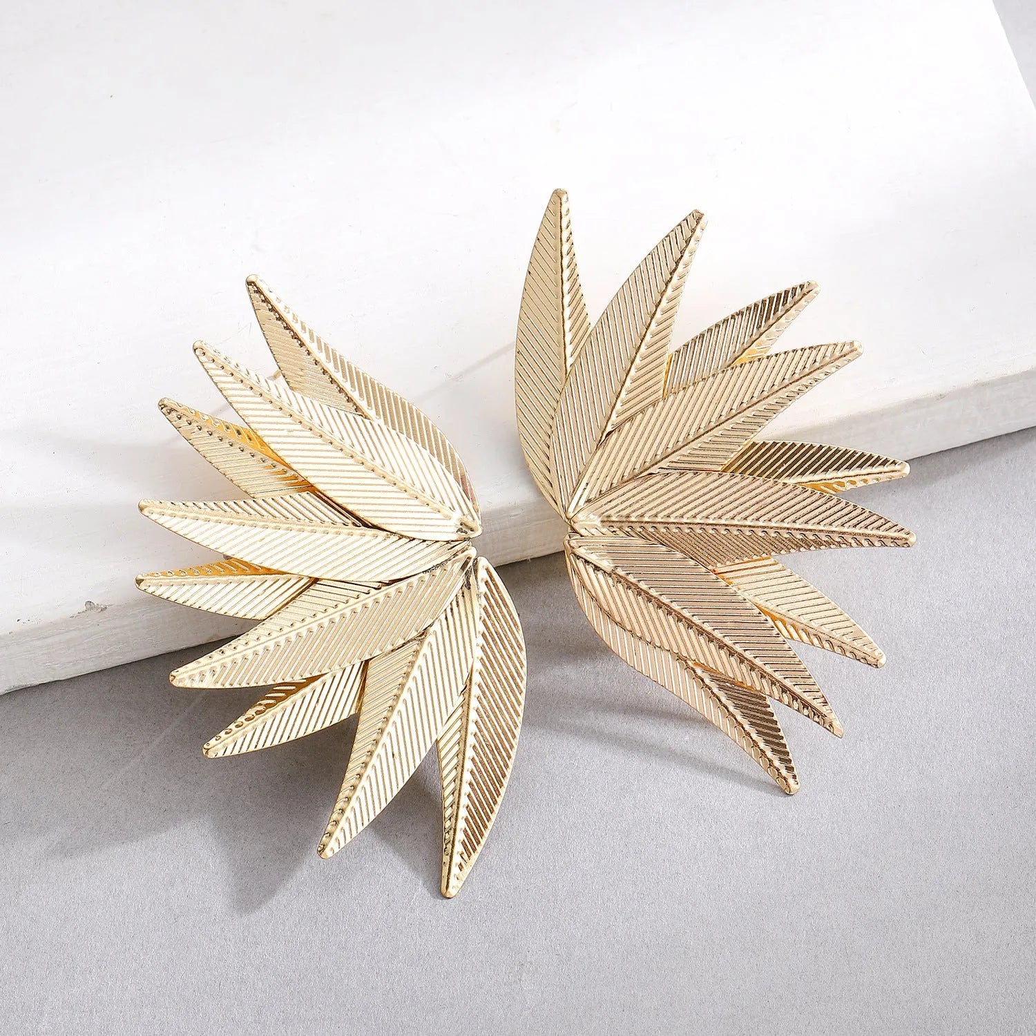 Gold and white leaf-shaped patch earrings made of alloy metal on a neutral background