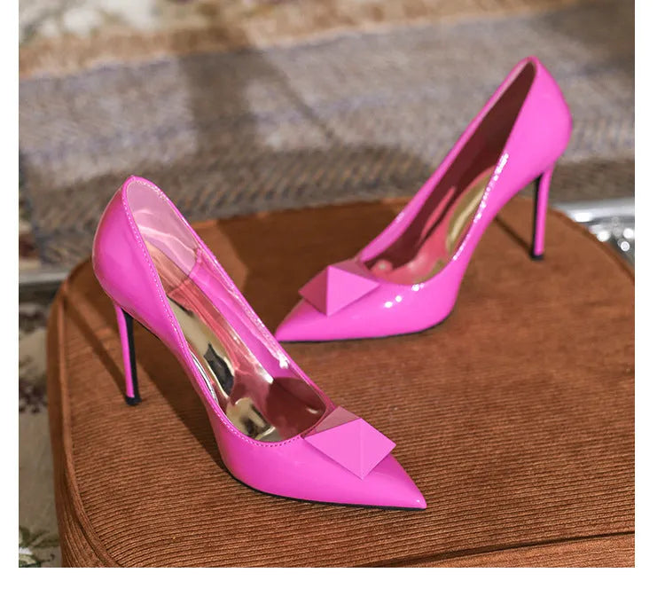 Pink women's patent leather pointed toe stiletto high heels with a buckle, on a white background.